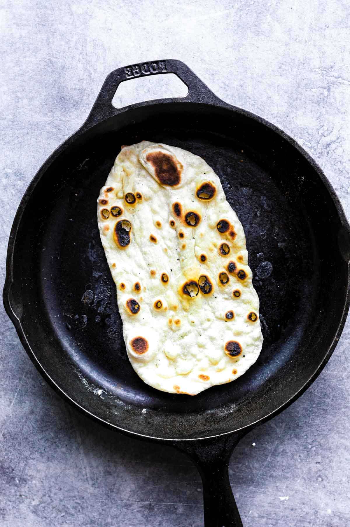 Charred naan in a cast-iron skillet.