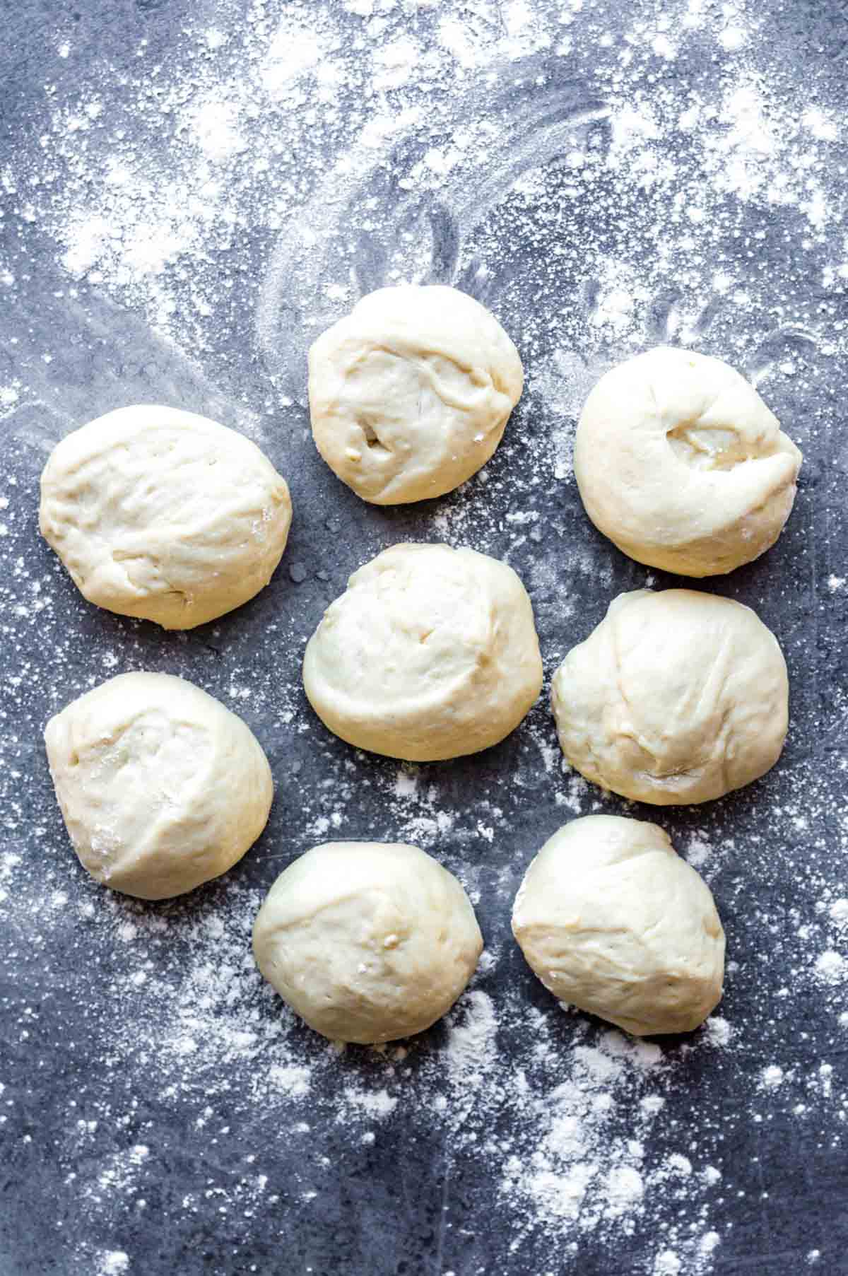 8 dough balls on a countertop with sprinkled flour.