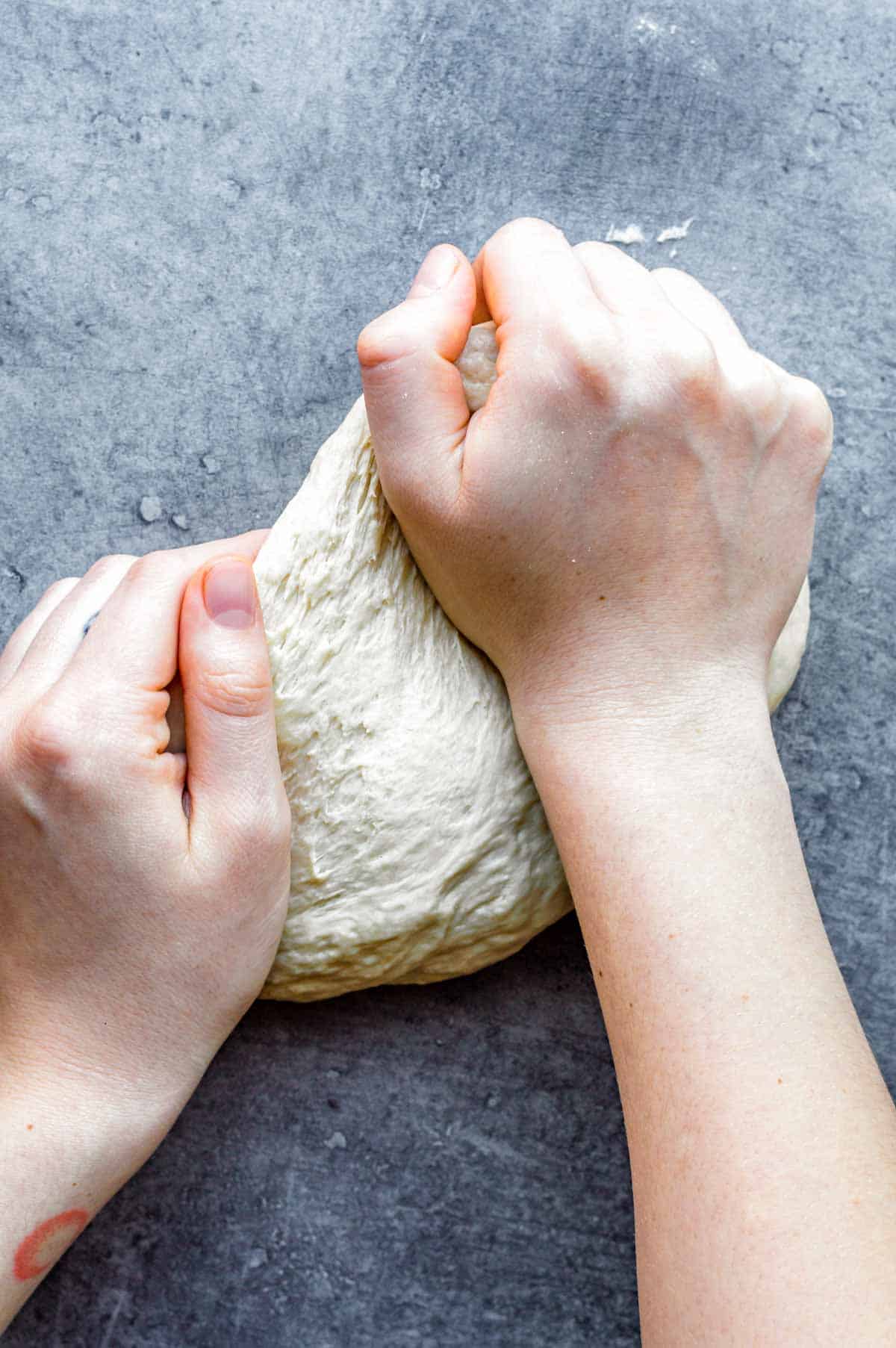 Two hands kneading dough on a kitchen countertop.