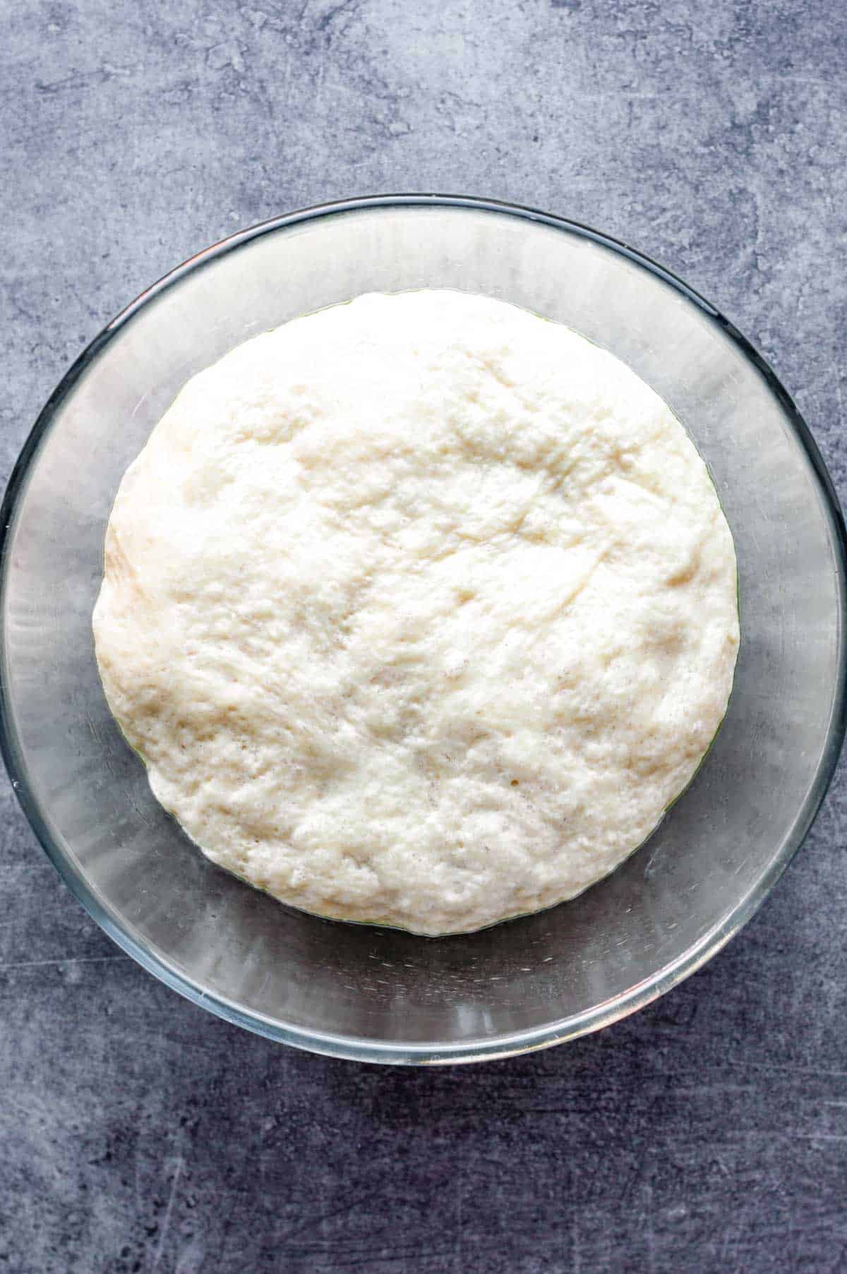 Risen dough in a glass bowl on a kitchen countertop.