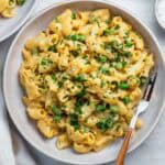 Vegan mac and cheese sprinkled with parsley, served on a plate, with a fork placed on the right side.