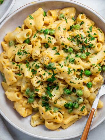 Vegan mac and cheese sprinkled with parsley, served on a plate, with a fork placed on the right side.